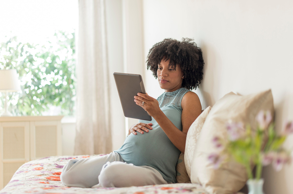 Pregnant African American mother using digital tablet in bed
