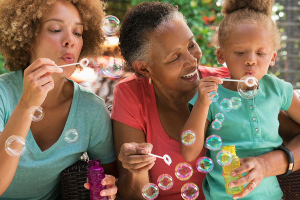 Black multi-generation family blowing bubbles outdoors
