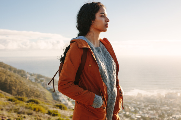 Young woman standing with her hands in pocket of her jacket and looking away. African american female standing on a mountain and looking at a view.