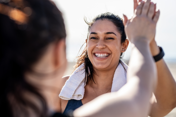 Smiling woman giving high five to her friend after exercising. Woman looking happy after a successful workout session outdoors.