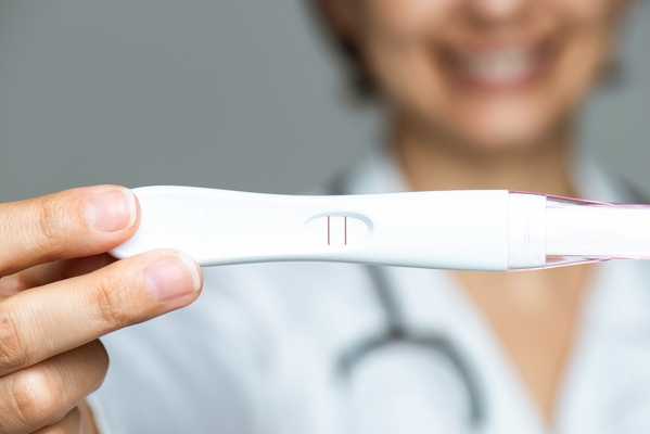 Unrecognizable female doctor is showing an unused pregnancy test to camera with a toothy smile.